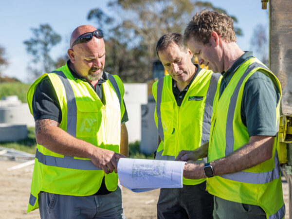 Three men in high viz vests discussing architectural plans on a site