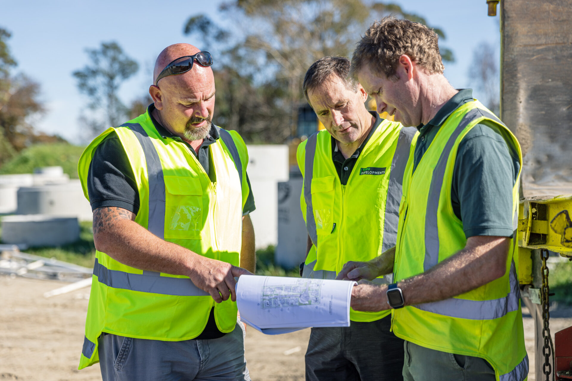 Three men in high viz vests discussing architectural plans on a site